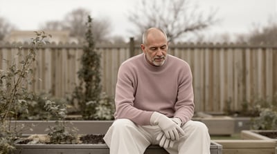 A man sits on the edge of a raised garden bed holding gardening gloves