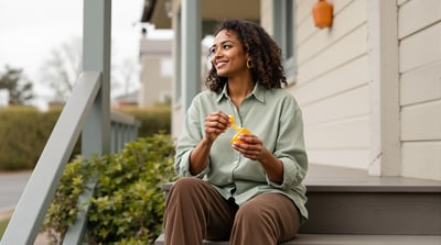 A woman sits on the front steps of a house peeling an orange