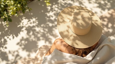 A person seen from above resting in dappled garden shade wearing a wide-brimmed straw sun hat