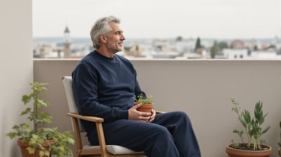 A man sits on a small balcony holding a pot of seedlings