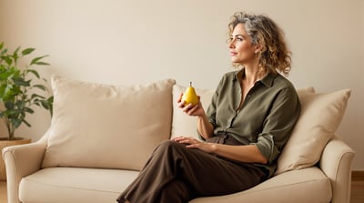 A woman sits on a sofa in a quiet living room holding a pear