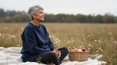 A woman sits on a blanket in a meadow beside a basket of apples