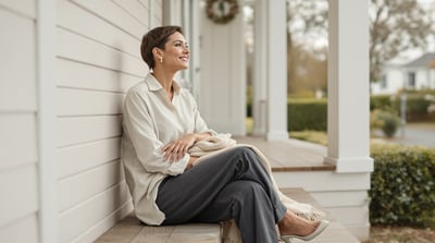 A woman sits on the front steps of a house with a folded scarf