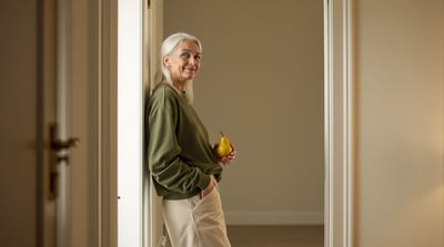 A woman stands in an open doorway holding a pear